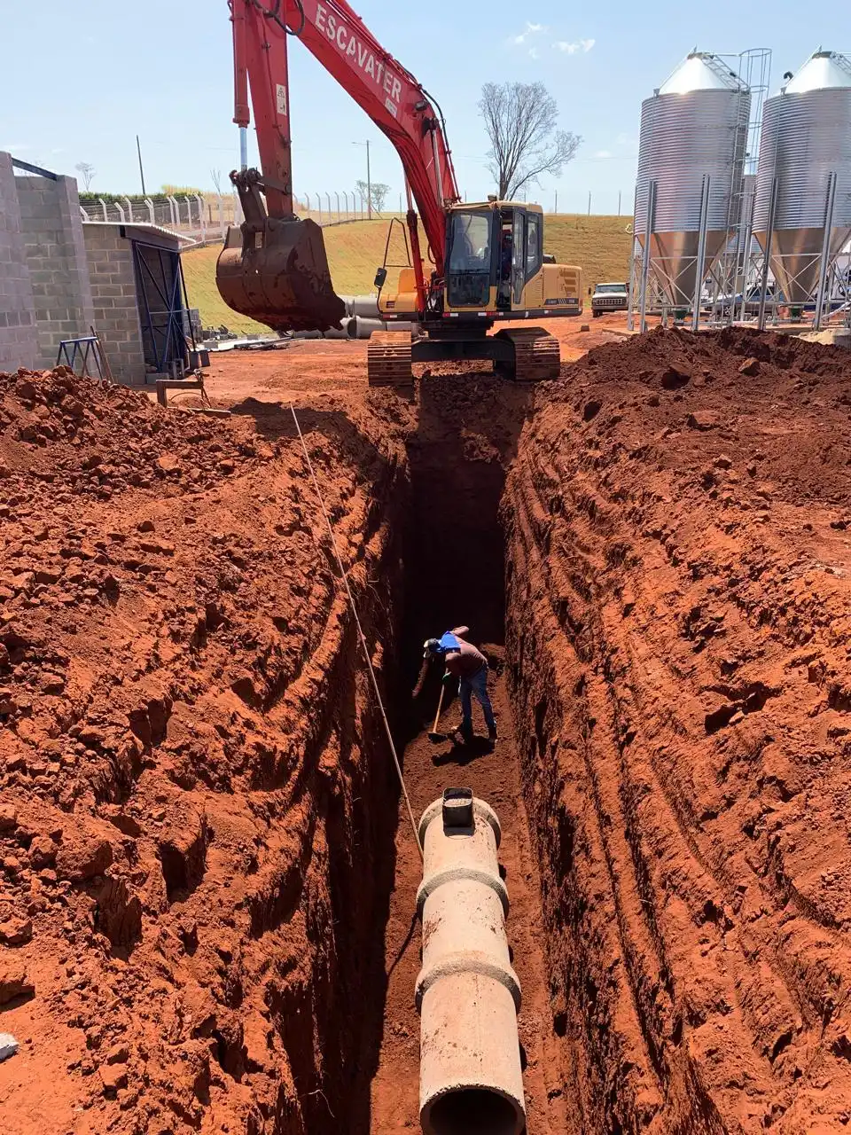 Escavadeira executando vala para drenagem com tubos de concreto